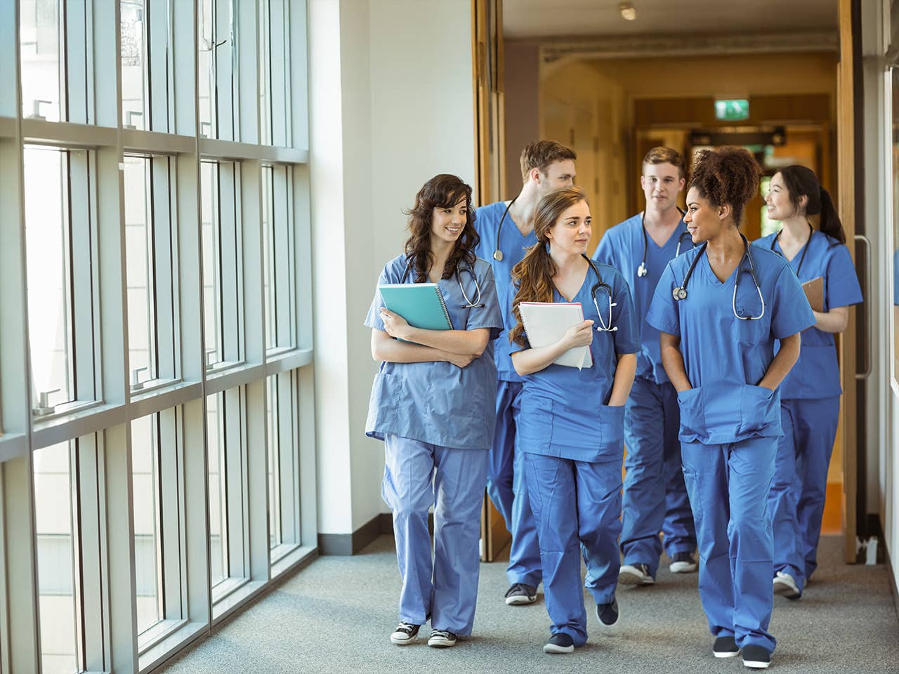 A group of medical students in scrubs walking in a hallway, engaged in conversation.