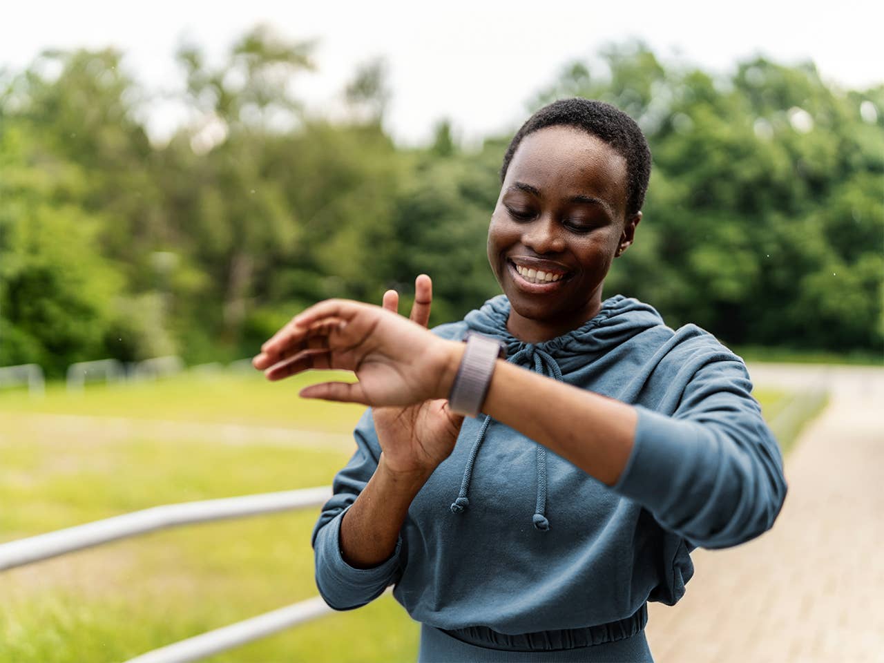 Smiling Black woman with short black hair standing outside while looking at watch on her wrist