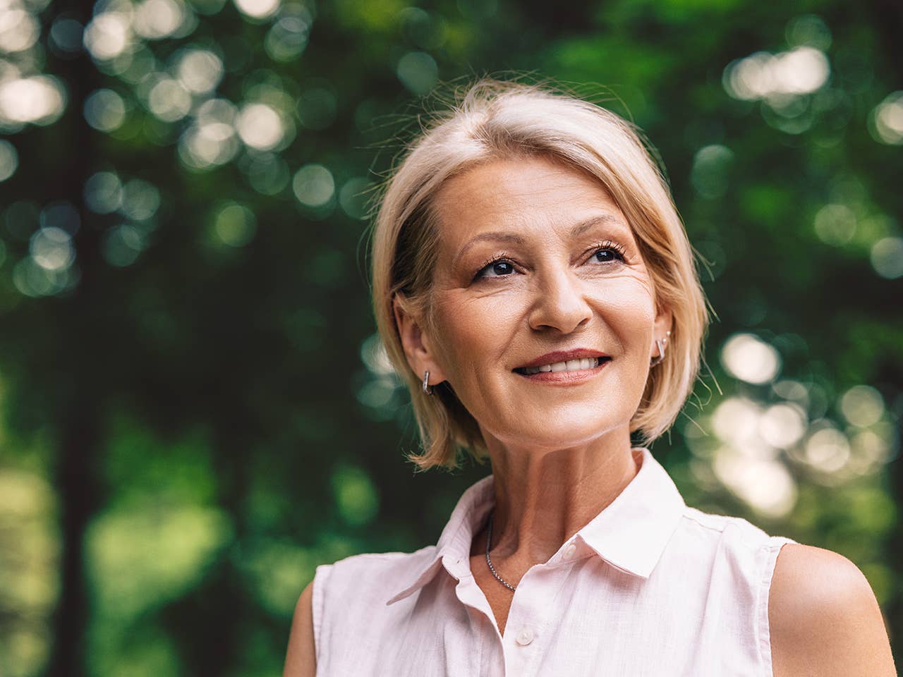 Smiling white woman stands in front of trees, looking into the distance