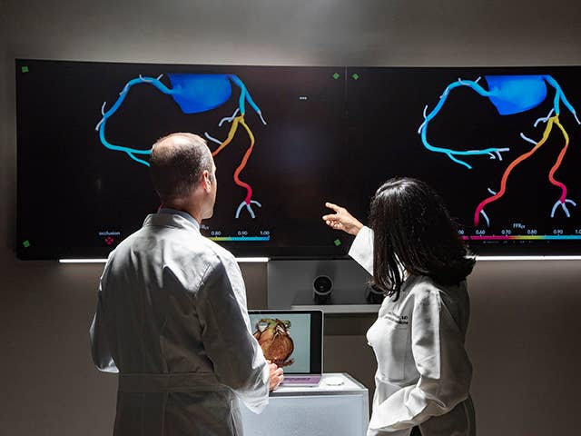 Two doctors examining a computer screen displaying a heart graphic, engaged in a discussion about patient care.