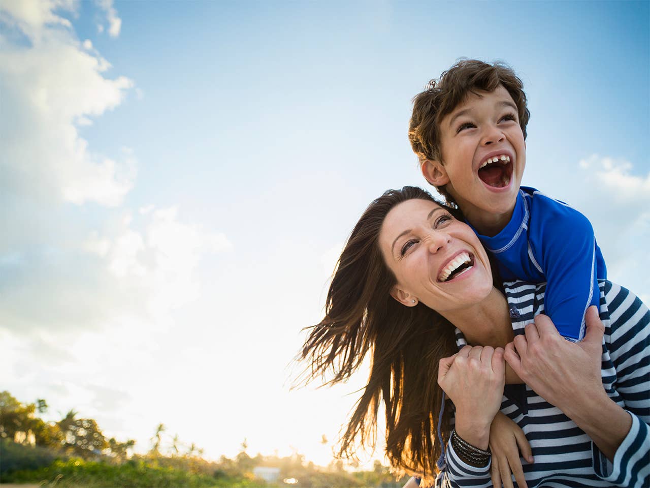 Smiling mother with laughing young son on her back in the sunshine