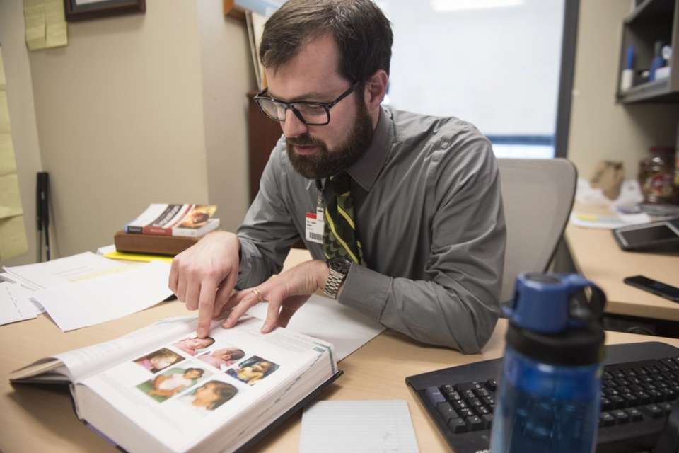 Doctor sits at his desk and points at page of a medical book