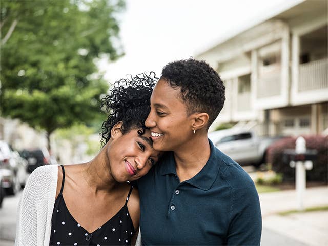 Young Black woman smiles as she rests her head on the shoulder of her partner