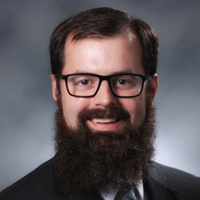 A bearded man in glasses wearing a suit, identified as Dr. Caleb Bupp, Clinical Director at Helen DeVos Children’s Hospital.