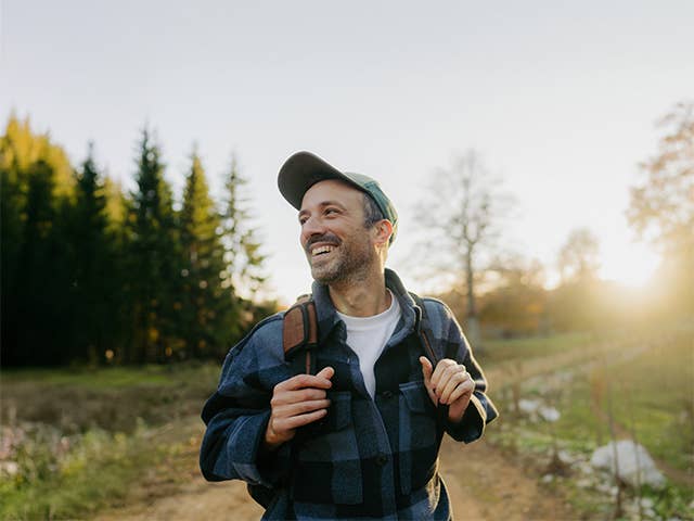 Smiling middle aged white man stands in the evening sun while hiking outdoors