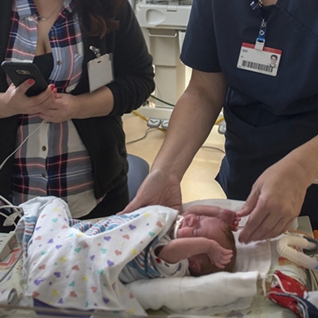 Mother and a nurse reach down to touch a baby in the neonatal intensive care unit