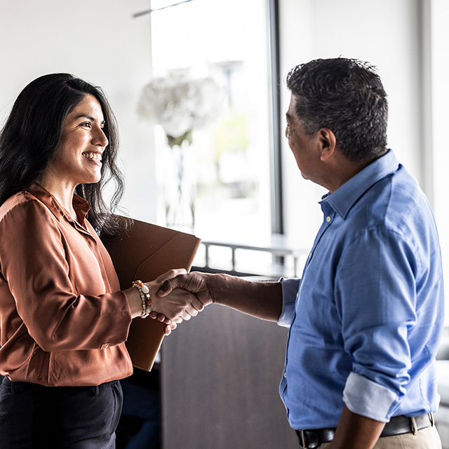 A man and woman shaking hands in a modern office setting.
