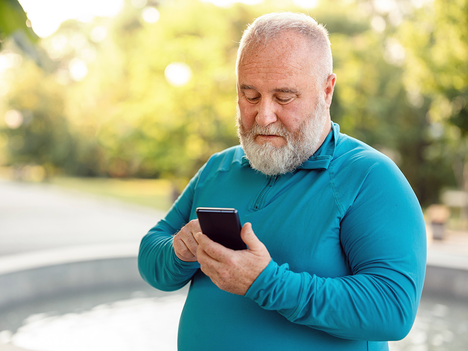 Middle aged white man looks at his phone while standing outdoors in workout clothes