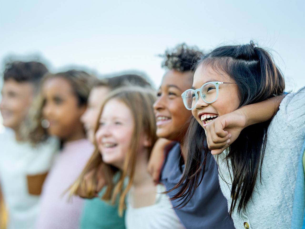 Group of six smiling boys and girls standing side-by-side outdoors