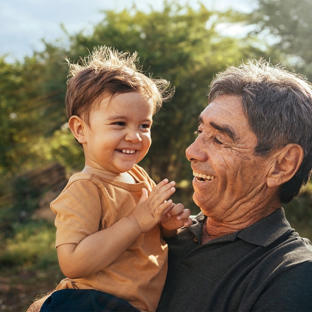 older man holding a young boy smiling while they are outside