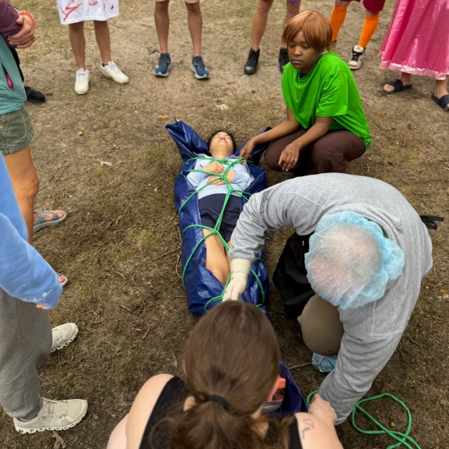 Residents participating in and watching an outdoor medical rescue during a wilderness retreat