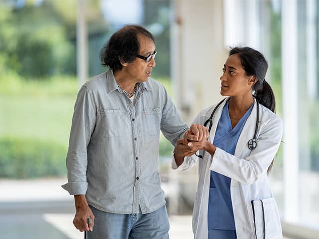 A doctor and patient stroll through a hospital corridor, engaged in conversation about medical care.