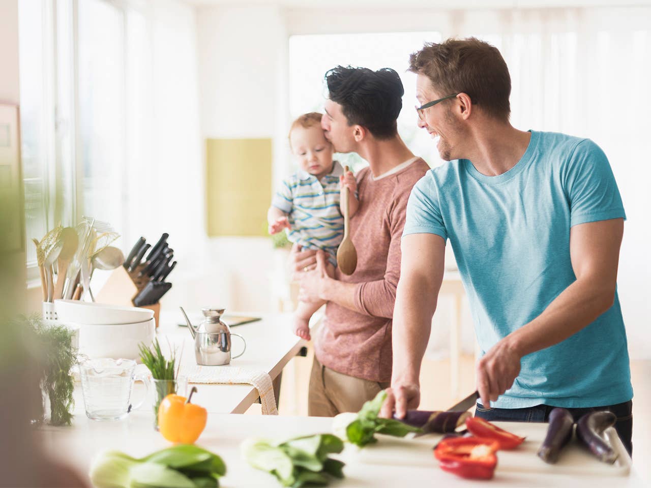Two men cooking in kitchen, as one holds a toddler