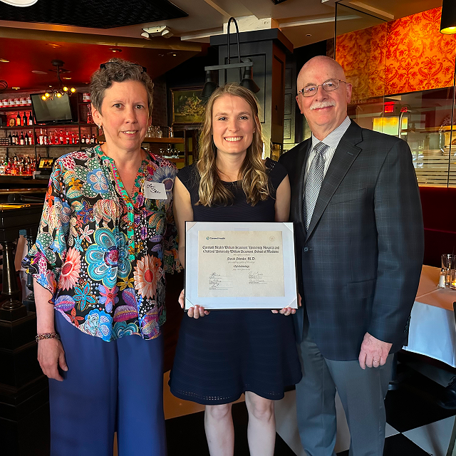 Certificate recipient posing with two presenters while holding a framed award certificate