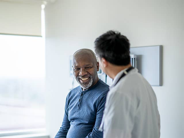 Smiling middle aged Black man speaks with a Corewell Health ear, nose, and throat surgeon in an exam room