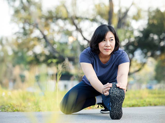Young Asian woman stretches her leg outdoors in the sunshine before jogging