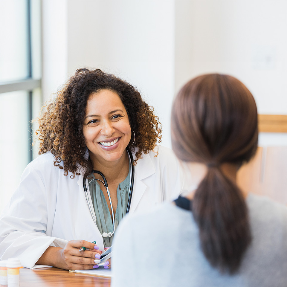 Smiling female doctor in a white lab coat sits across from a female patient