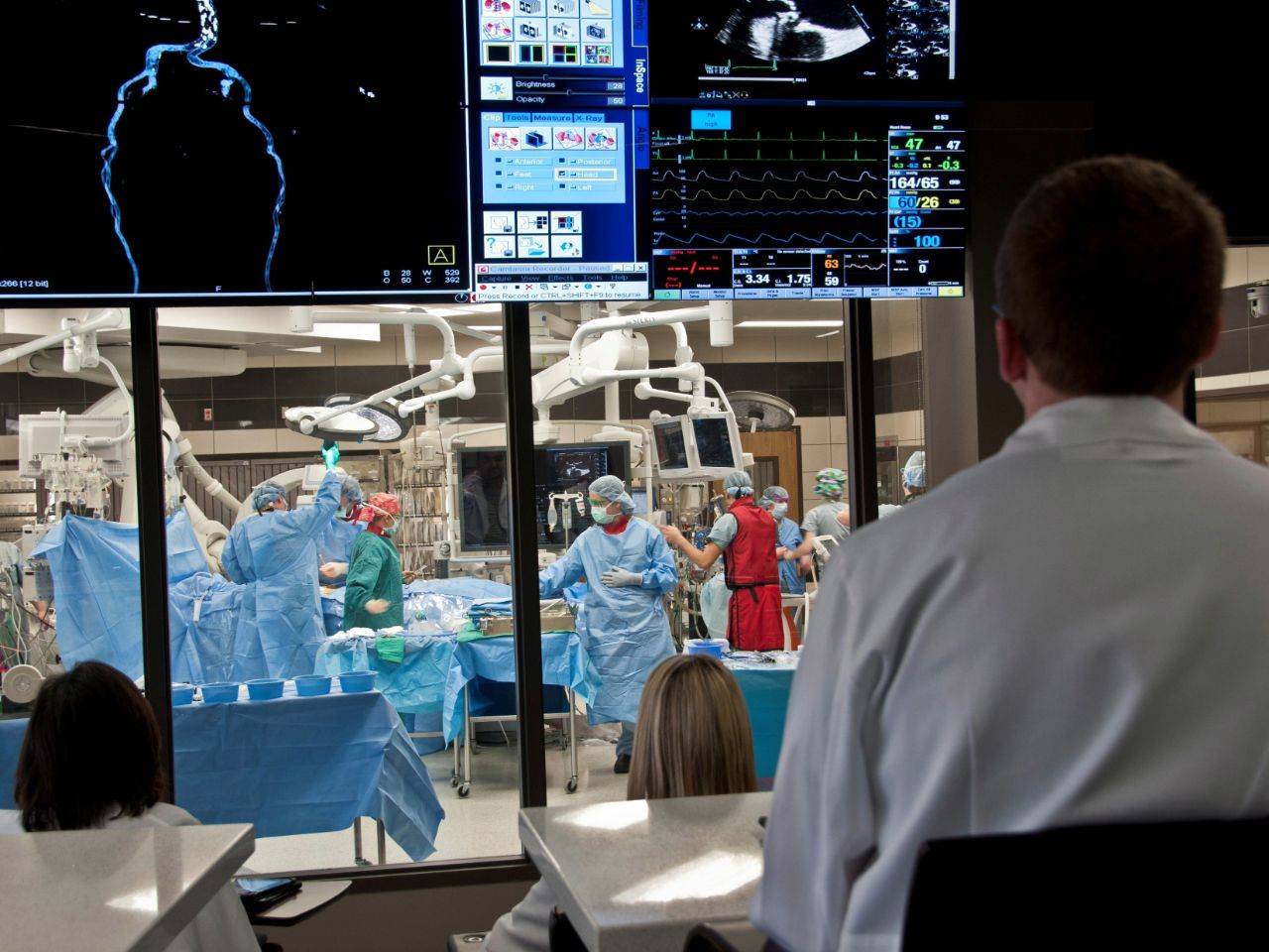Residents in an observation room watching a surgery in action through glass windows