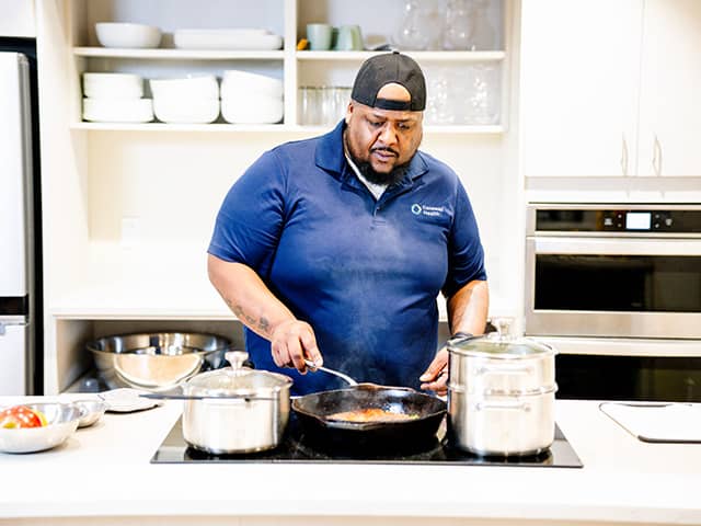 A man stirring a pot on the stove in a modern kitchen, surrounded by fresh ingredients and cooking utensils.