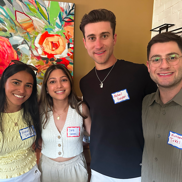 Four attendees pose together indoors at a community gathering, wearing name tags.