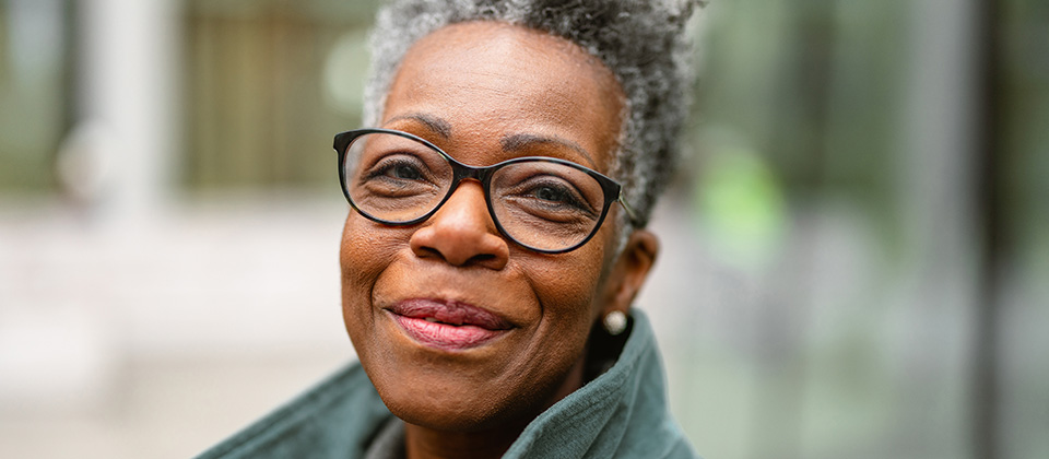 An older woman wearing glasses and a green jacket smiles warmly.