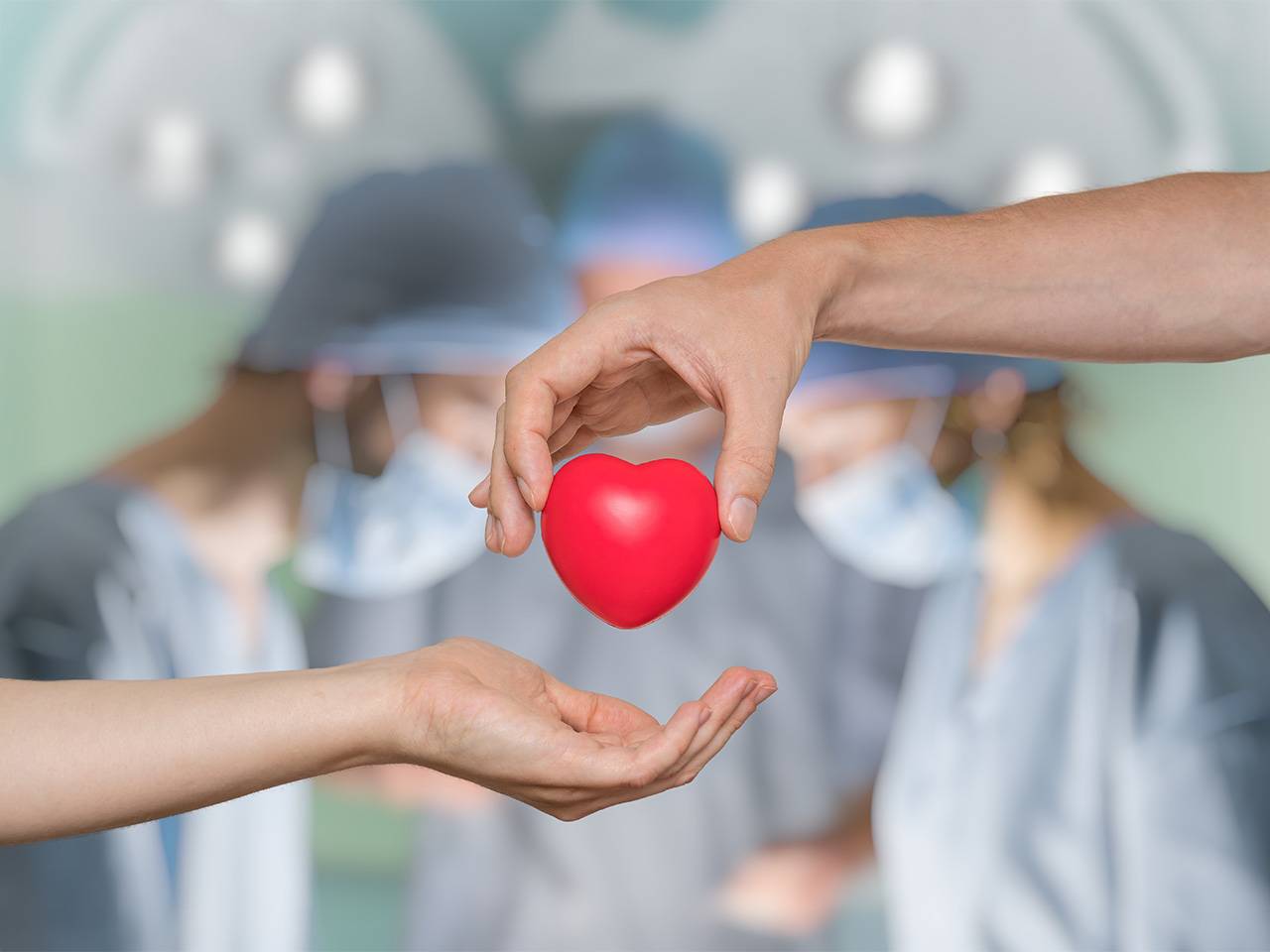 Graphic of one hand holding a cartoon heart above another with surgeons in the background
