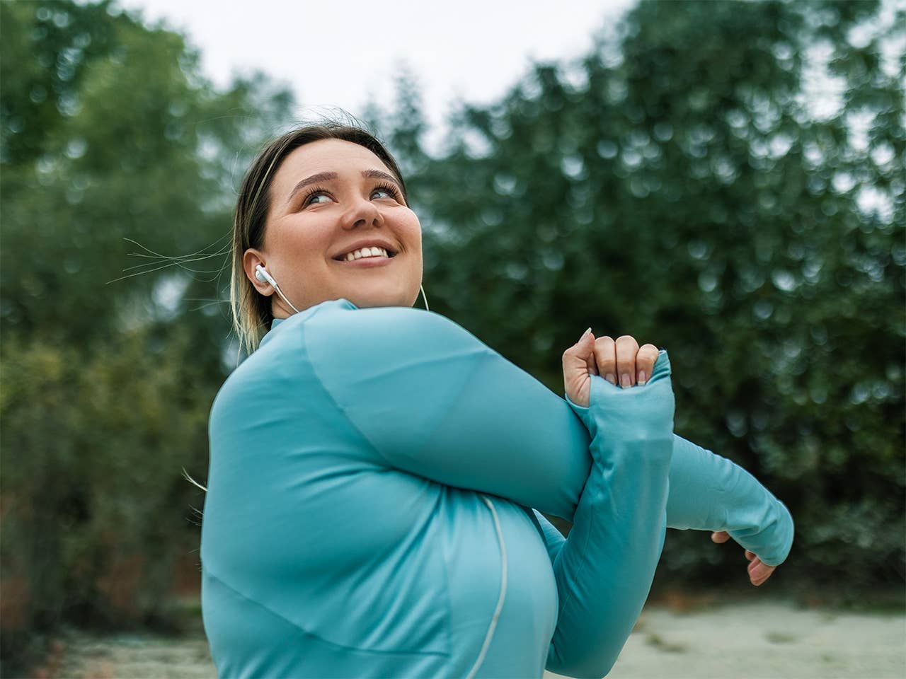 Woman in teal jacket stretches her arms