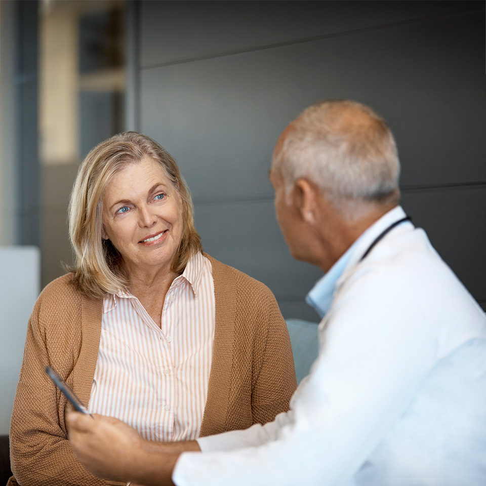 Older woman with shoulder length grey hair sits and speaks with doctor