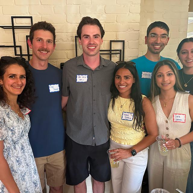 Seven attendees wearing name tags pose together indoors at a community gathering.