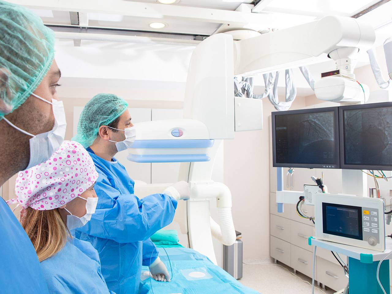 Medical team in a cardiac catheterization lab viewing imaging monitors during an interventional cardiology procedure.