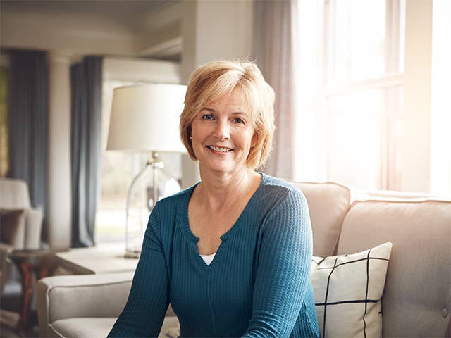 White woman in a teal sweater smiles while she sits in a sun filled room