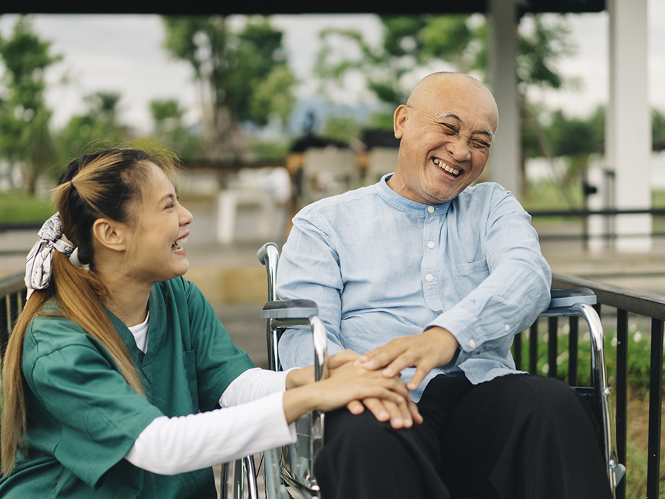 A man in a wheelchair smiling in a pleasant outdoor setting.
