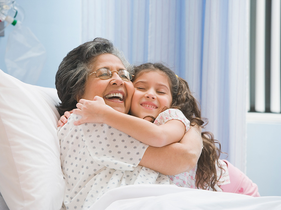 older female patient in her hospital bed being hugged by a little girl visiting her