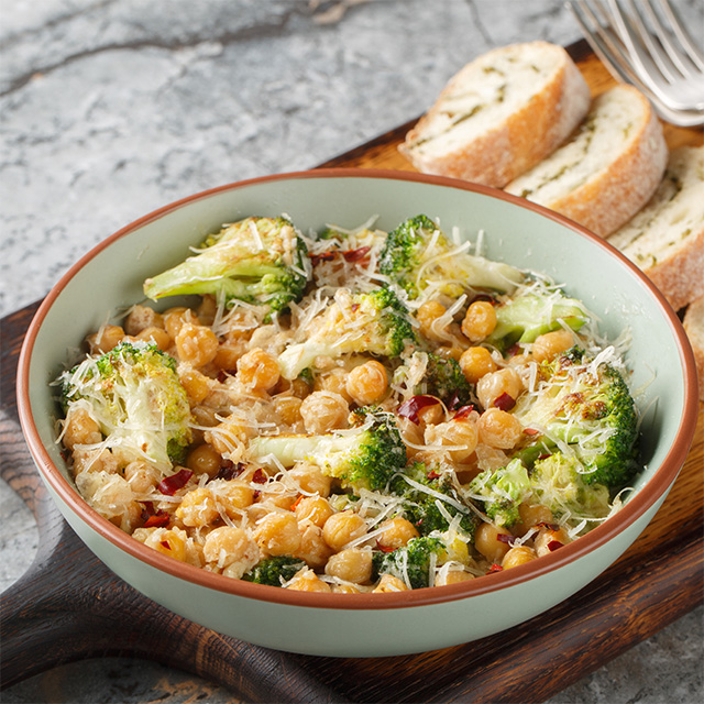 Bowl of cheesy chickpea and broccoli bake topped with grated cheese, served as a hearty plant-based meal.