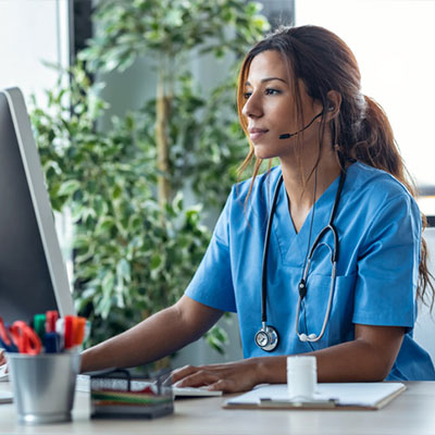 Woman in light blue scrubs sits in front of a computer