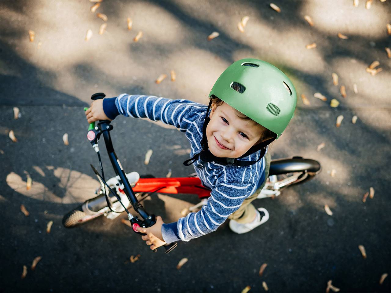 Smiling young boy wearing a blue and white striped shirt and green helmet sits on a bicycle outdoors