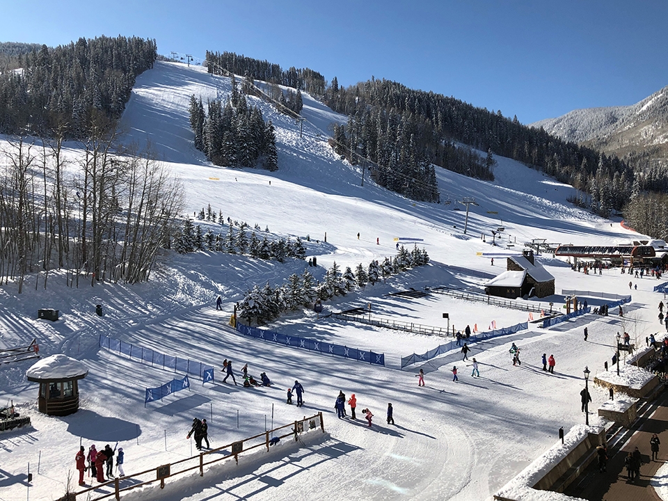A ski resort scene featuring people skiing and snowboarding on snowy slopes under a clear blue sky.