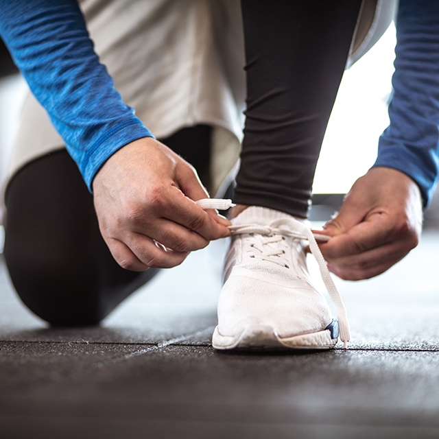 A person kneeling down, tying a white shoe on a sidewalk.