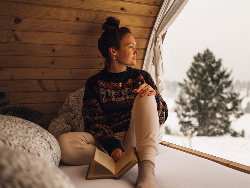 A woman comfortably seated on a bed, focused on reading a book.