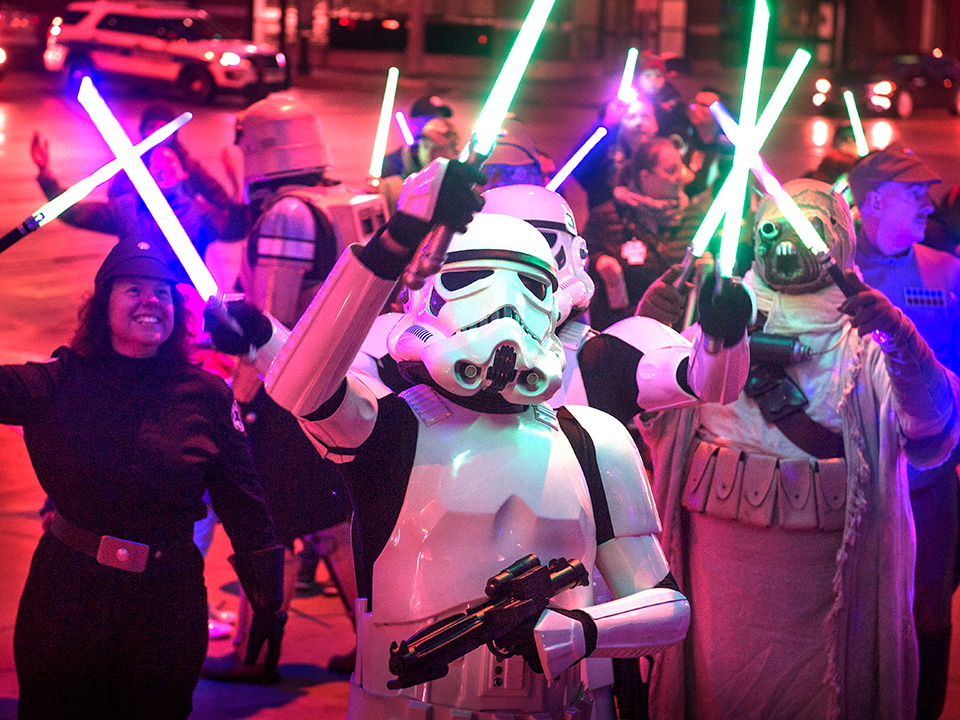 Project Night Lights at Corewell Health Helen DeVos Children's Hospital, a group of adults dressed as Star Wars characters standing outside in the dark with brightly lit lightsabers, supporting patients