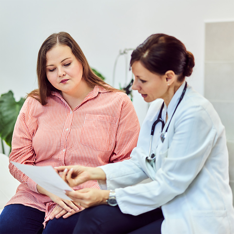 Woman in a pink shirt sits next to her doctor, looking at paperwork