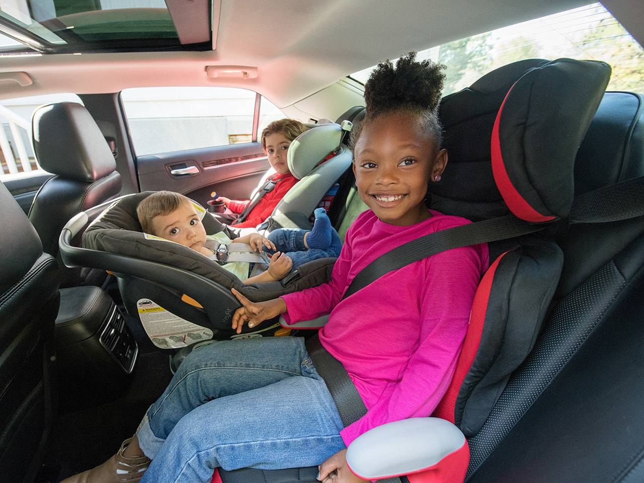 Three children sitting in car seats in the back seat of a vehicle