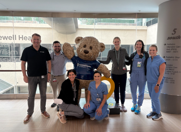 Staff members posing for a picture around a bear in a Corewell Health shirt in the hospital
