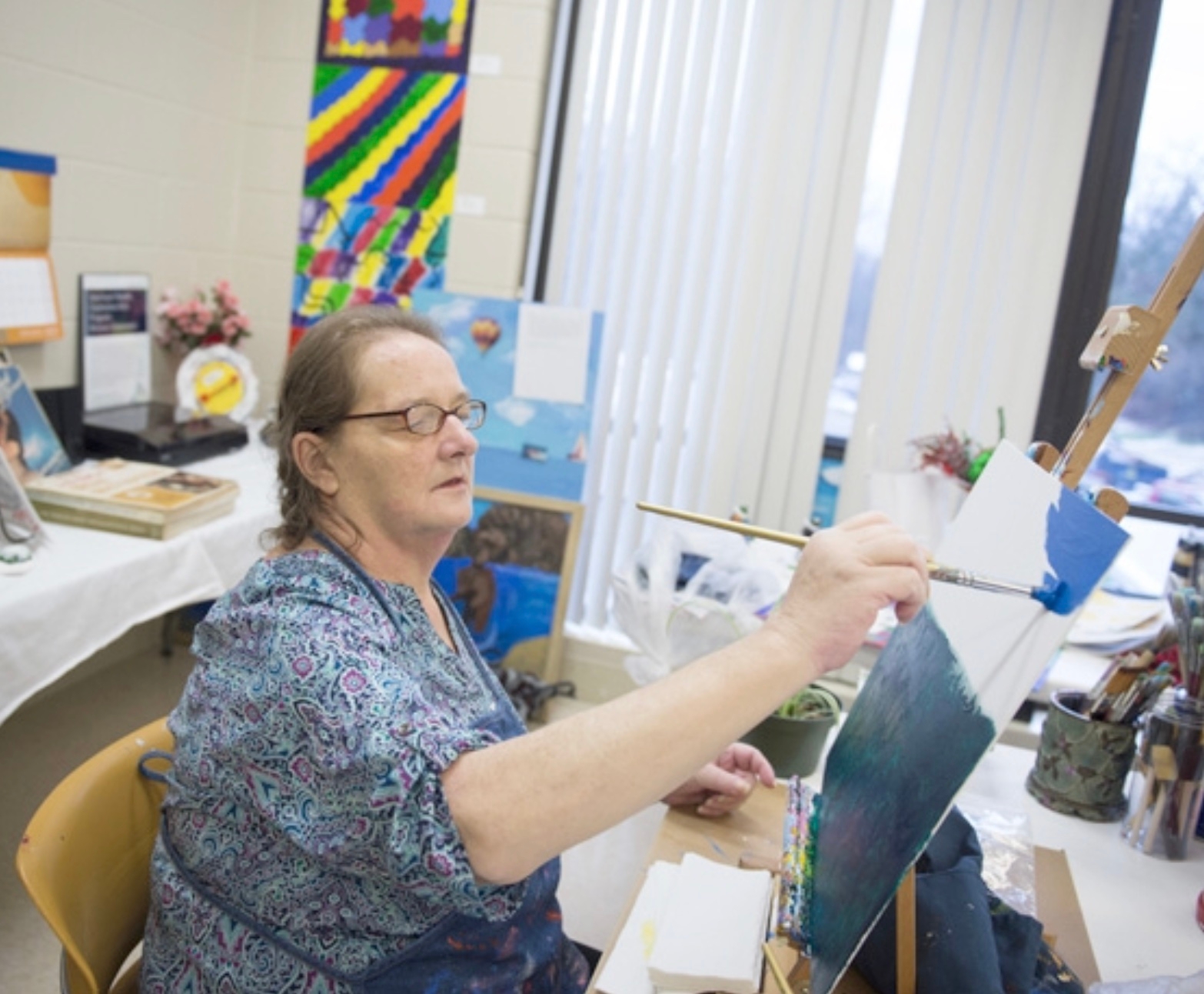 woman with glasses painting on a canvas