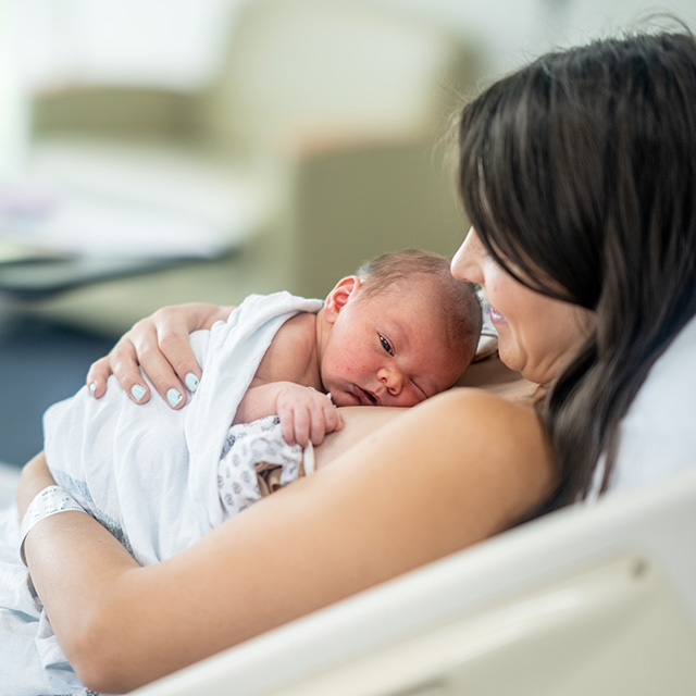 Woman in a hospital bed holds her newborn baby on her chest, during a skin-to-skin contact session