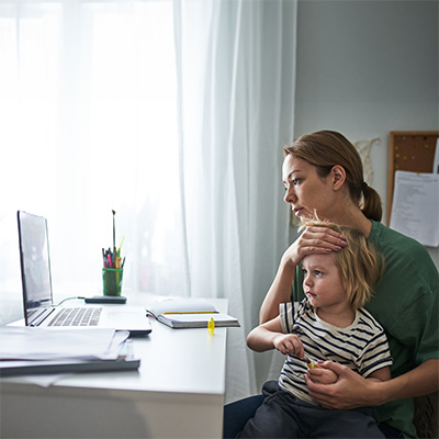 Young woman sits in front of laptop with toddler in her lap