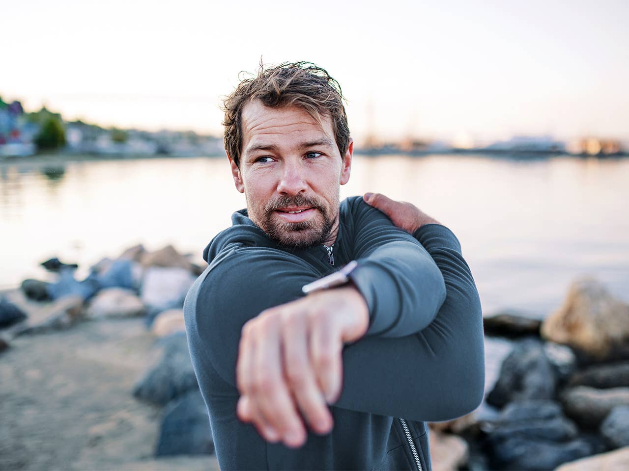 Man in wetsuit stands in front of lake stretching