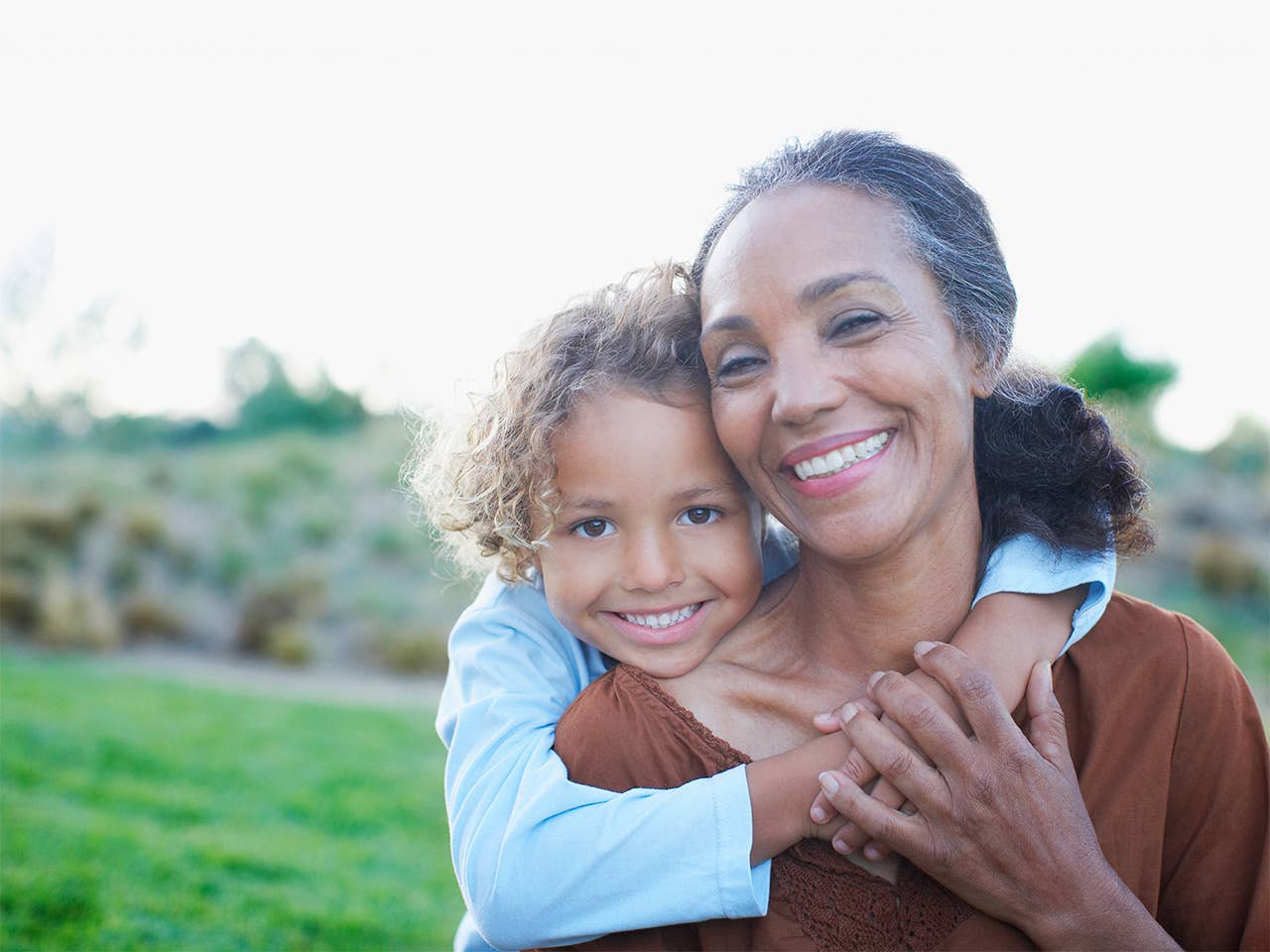 Smiling old Black woman gets a hug from her grandchild while they are outdoors