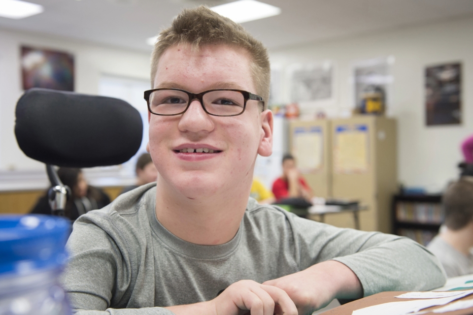 Preteen boy with glasses smiles in a classroom