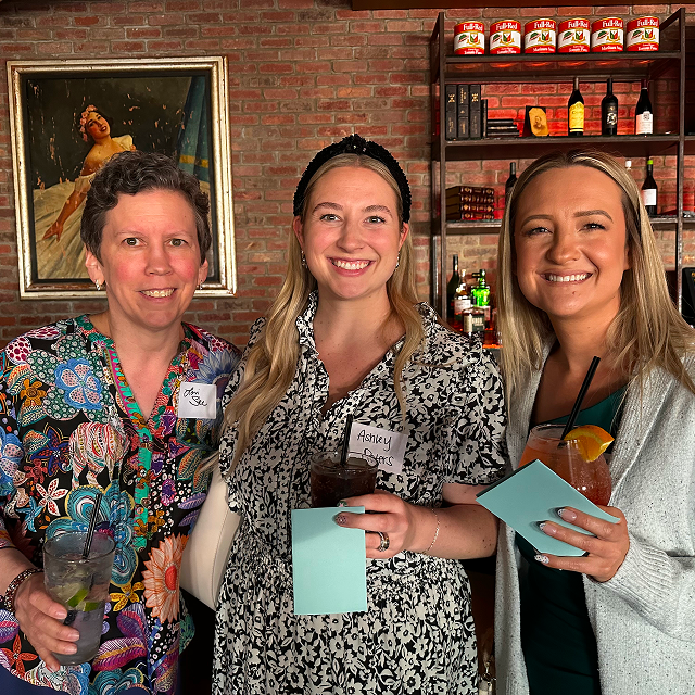 Three attendees posing together while holding drinks at a residency celebration dinner